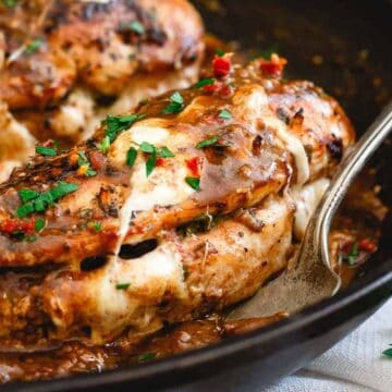 Cooked stuffed chicken breast with melted cheese and herbs, served in a cast iron skillet with a spoon. Parsley is sprinkled on top and visible on the side.