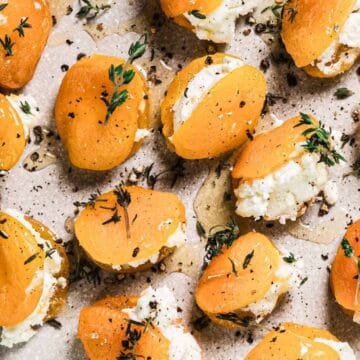 A plate of halved dried apricots stuffed with white cheese, garnished with fresh thyme and cracked black pepper, arranged on a round ceramic plate.