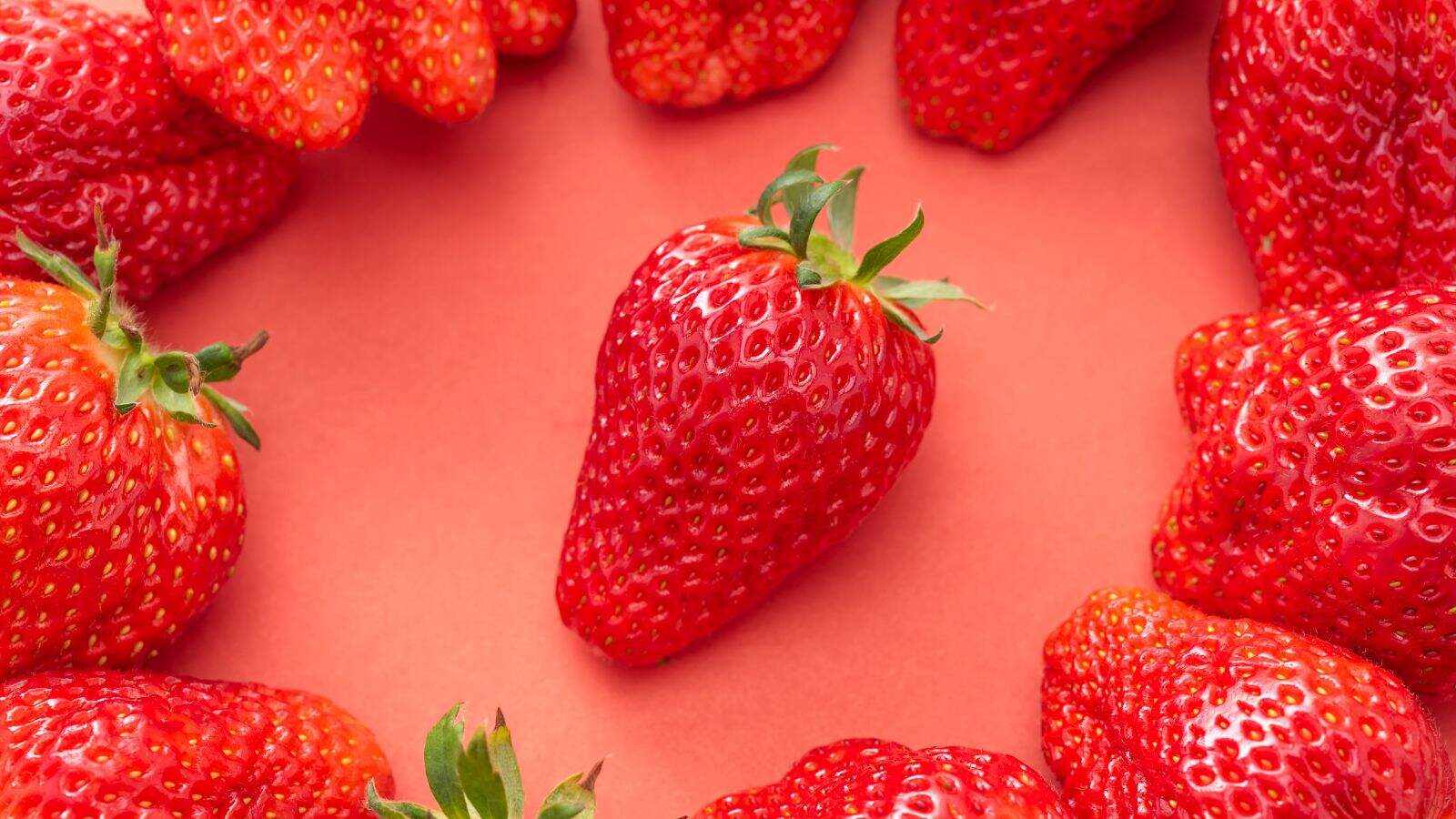Several strawberries are arranged in a circle on a red background, with one strawberry positioned in the center of the image.