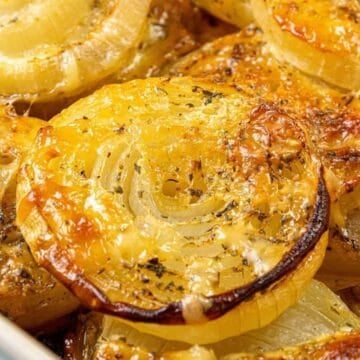Close-up of baked onion slices in a casserole dish, topped with herbs and caramelized to a golden brown.