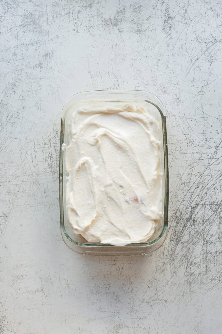 A rectangular glass dish filled with a smooth, white creamy substance, possibly yogurt or whipped cream, set on a scratched, light-colored surface.