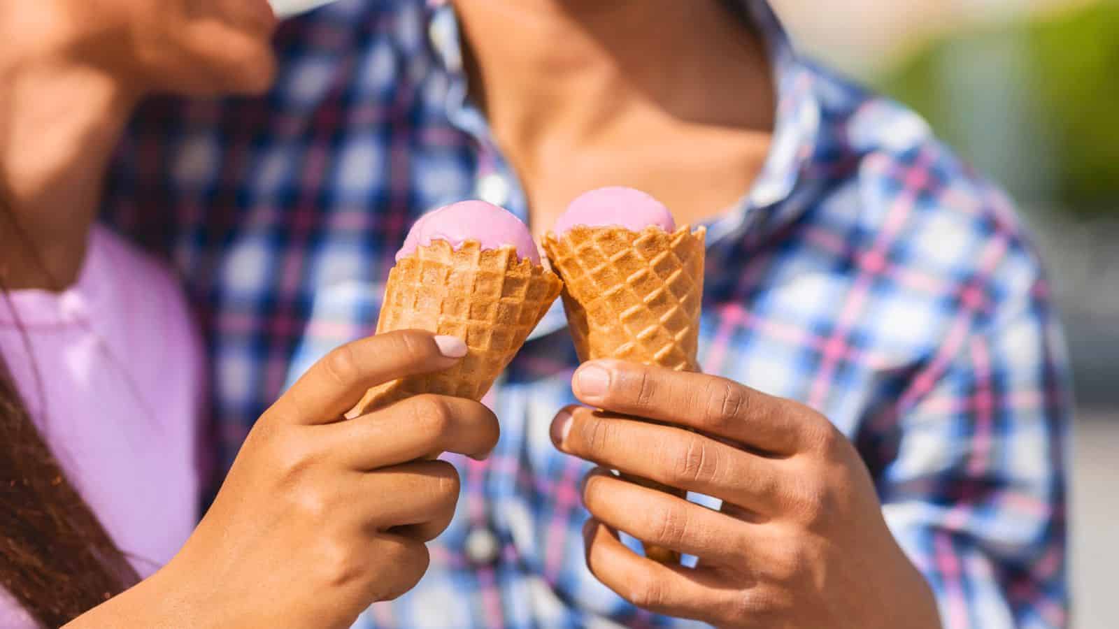 Two people holding ice cream cones with pink ice cream, standing close together. One person wears a plaid shirt, and the other wears a light-colored top. Their faces are partially out of frame.