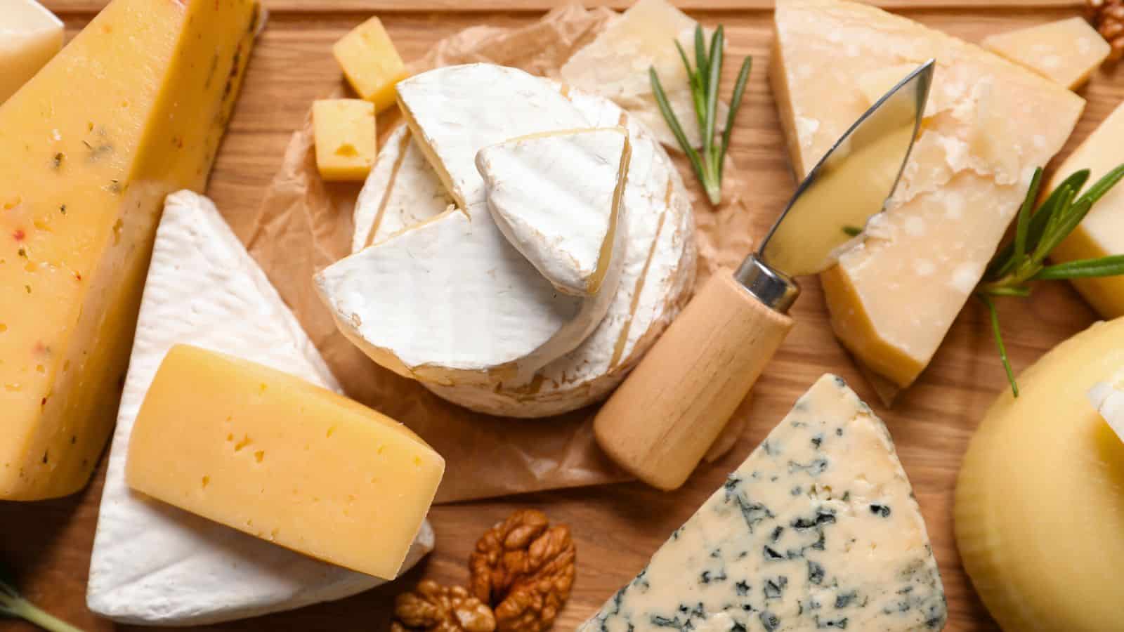 A wooden board topped with assorted cheeses, including brie, gouda, blue cheese, and parmesan, with a cheese knife, walnuts, and sprigs of rosemary.