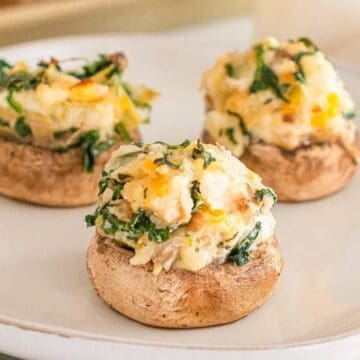Three stuffed mushrooms filled with a cheesy spinach mixture are served on a white plate, making them perfect go-to appetizers for any gathering.