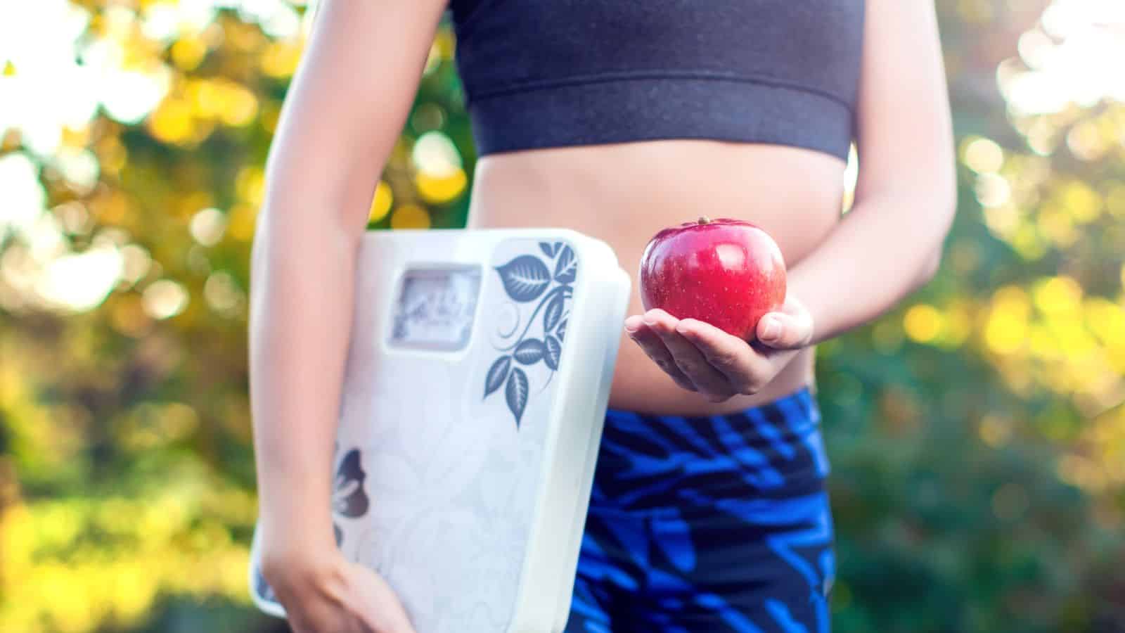 A person holding an apple and a scale.