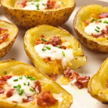 A plate of baked potato skins filled with melted cheese, bacon bits, sour cream, and chopped chives, arranged in a close-up view.