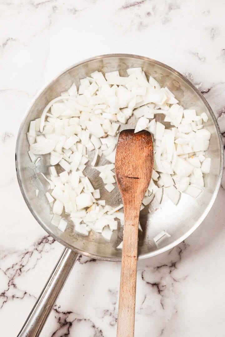 Chopped onions in a metal pan with a wooden spatula on a marble surface, perfect for starting your flavorful Chicken Borscht.