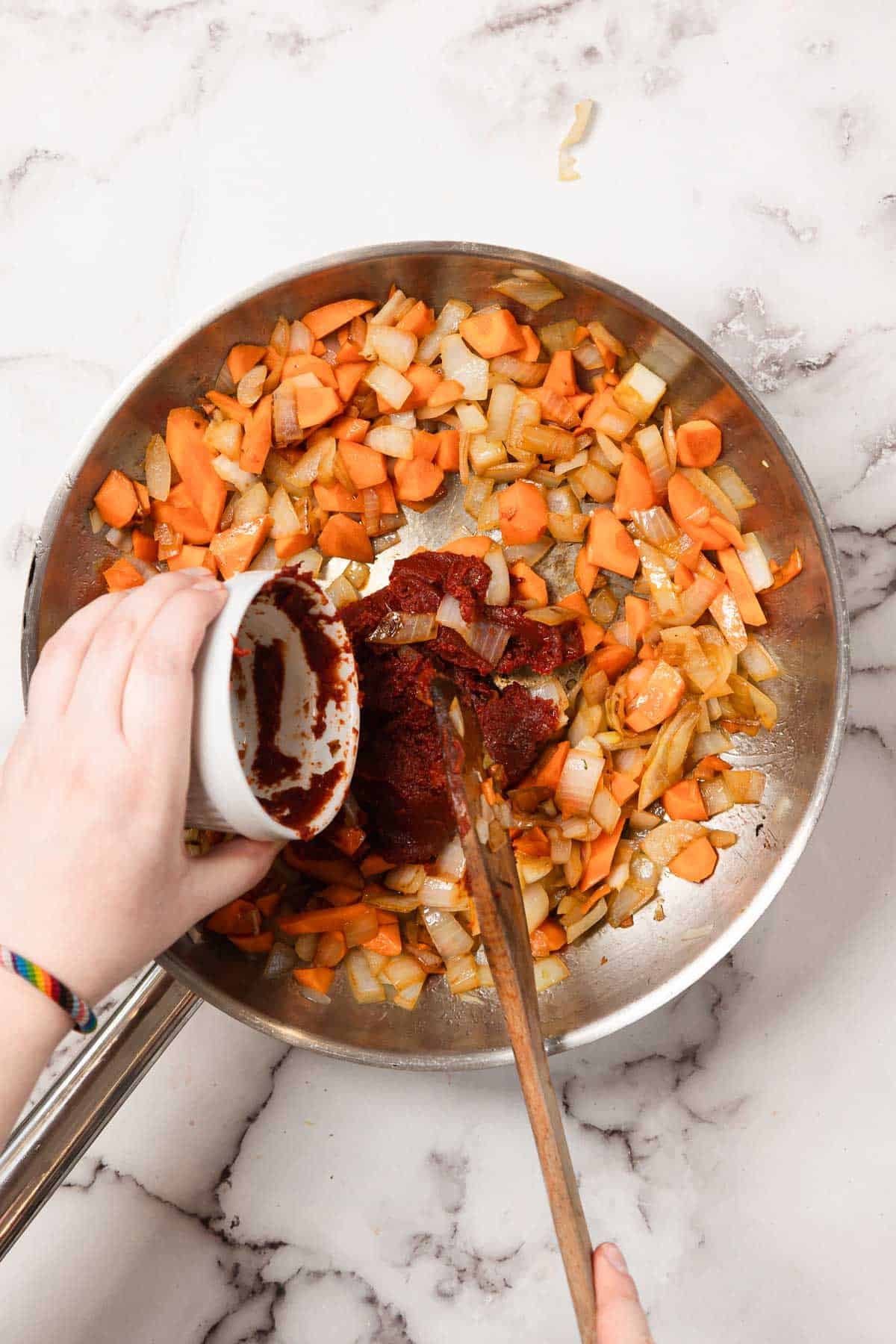 Chopped carrots and onions sizzle in a pan as tomato paste is added from a small bowl, forming the flavorful base for Chicken Borscht.
