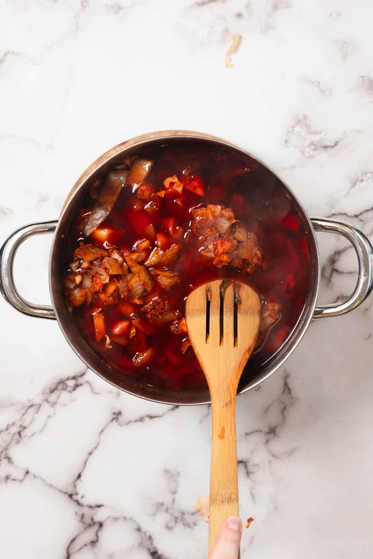 A pot of Chicken Borscht soup with a wooden spoon rests on a marble countertop, viewed from above.