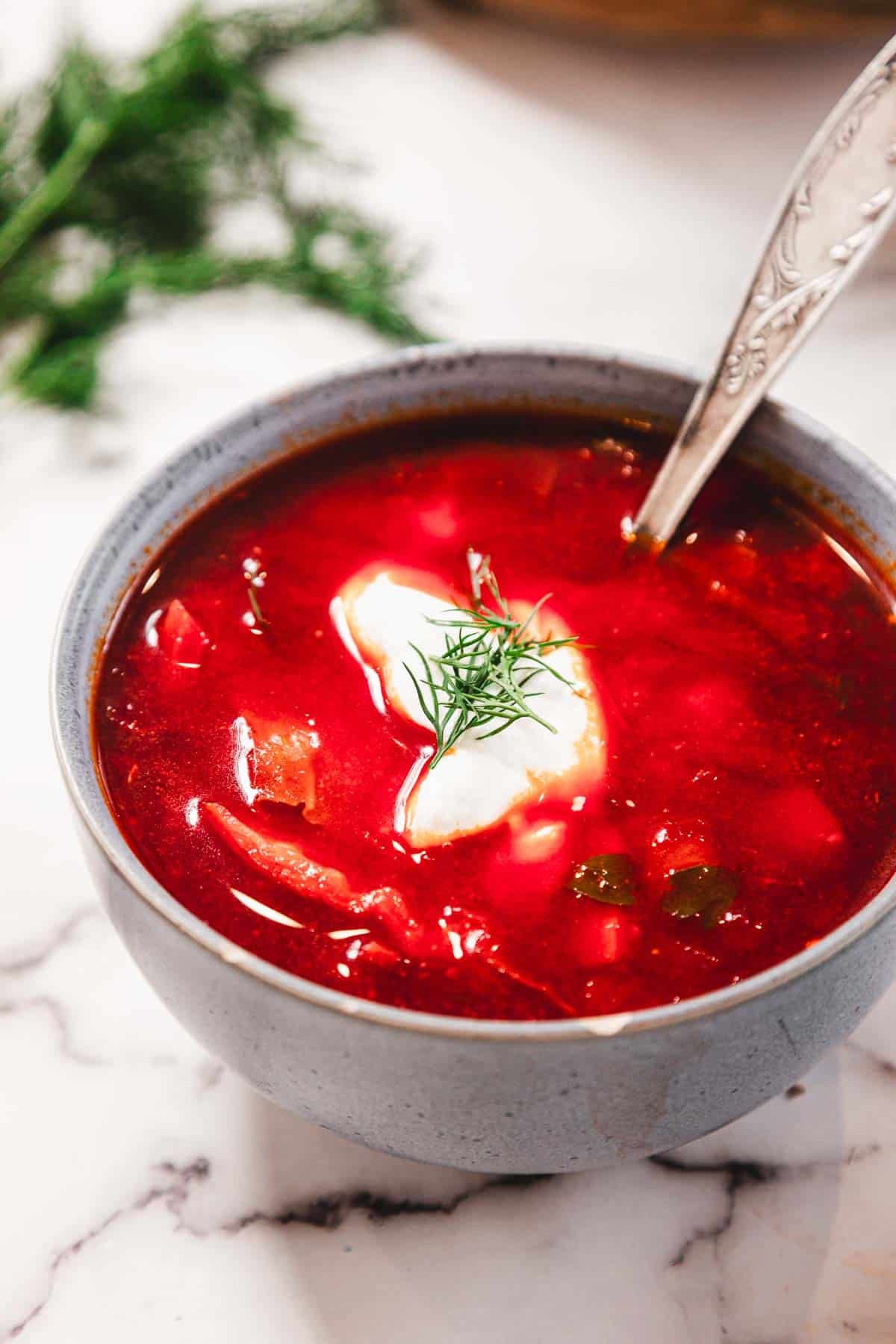 A bowl of vibrant red soup with sour cream and dill on top, with a spoon in the bowl.
