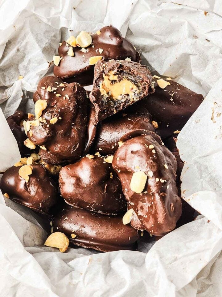 Chocolate-covered bars with a peanut butter filling, topped with chopped nuts, on crumpled parchment paper.