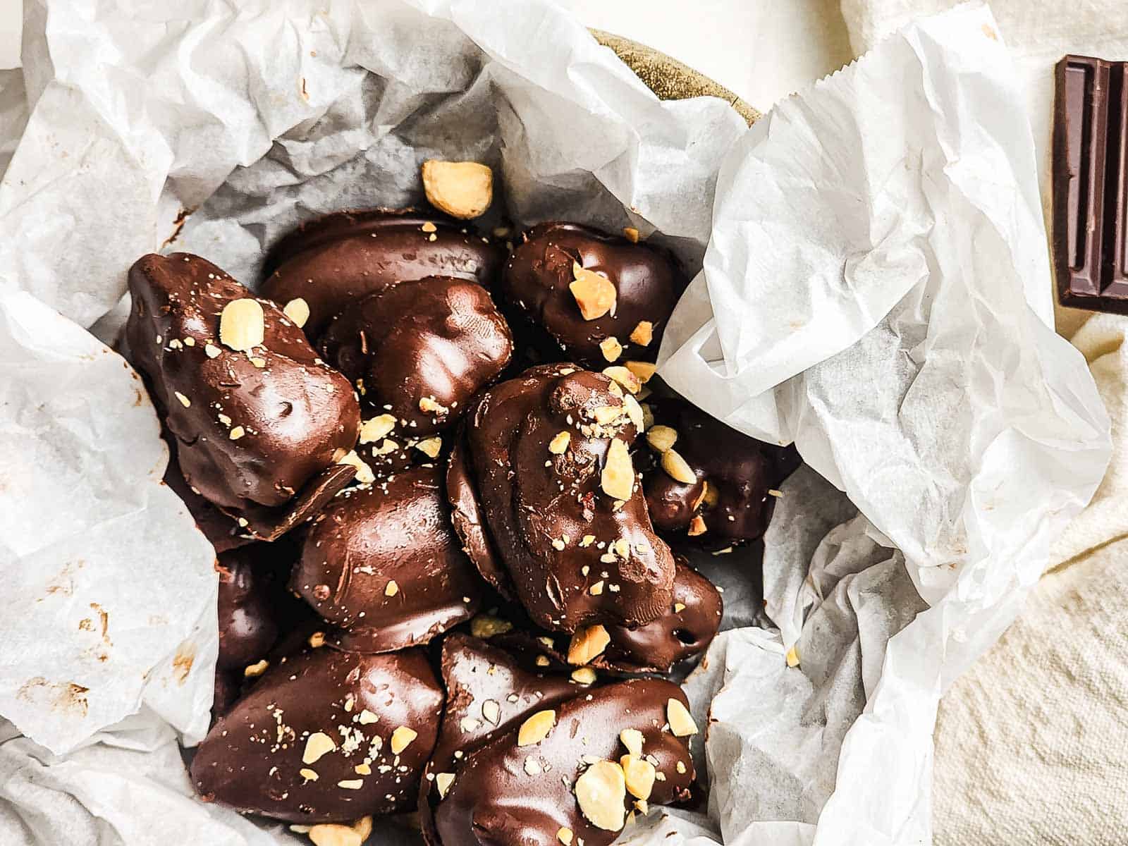 Chocolate-covered treats with chopped nuts in a parchment-lined bowl, viewed from above.