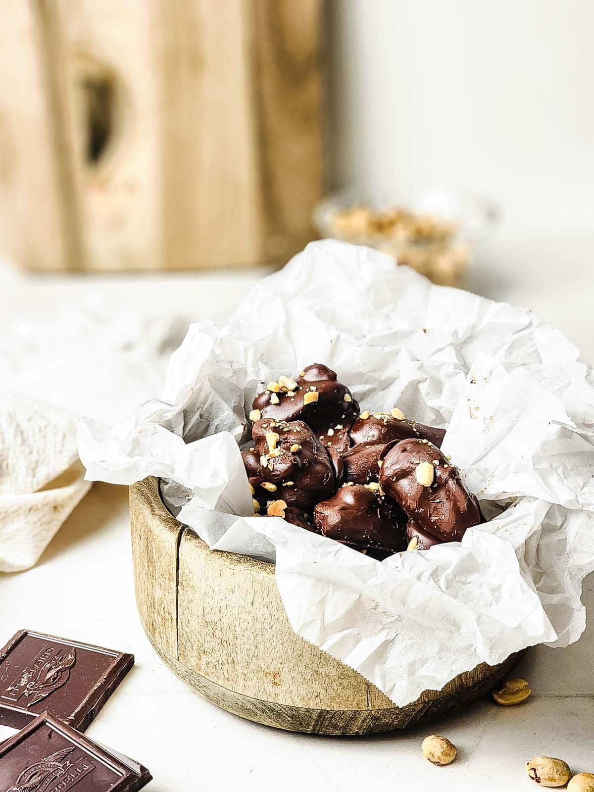 Chocolate-covered treats with nuts in a wooden bowl lined with crumpled white parchment paper.