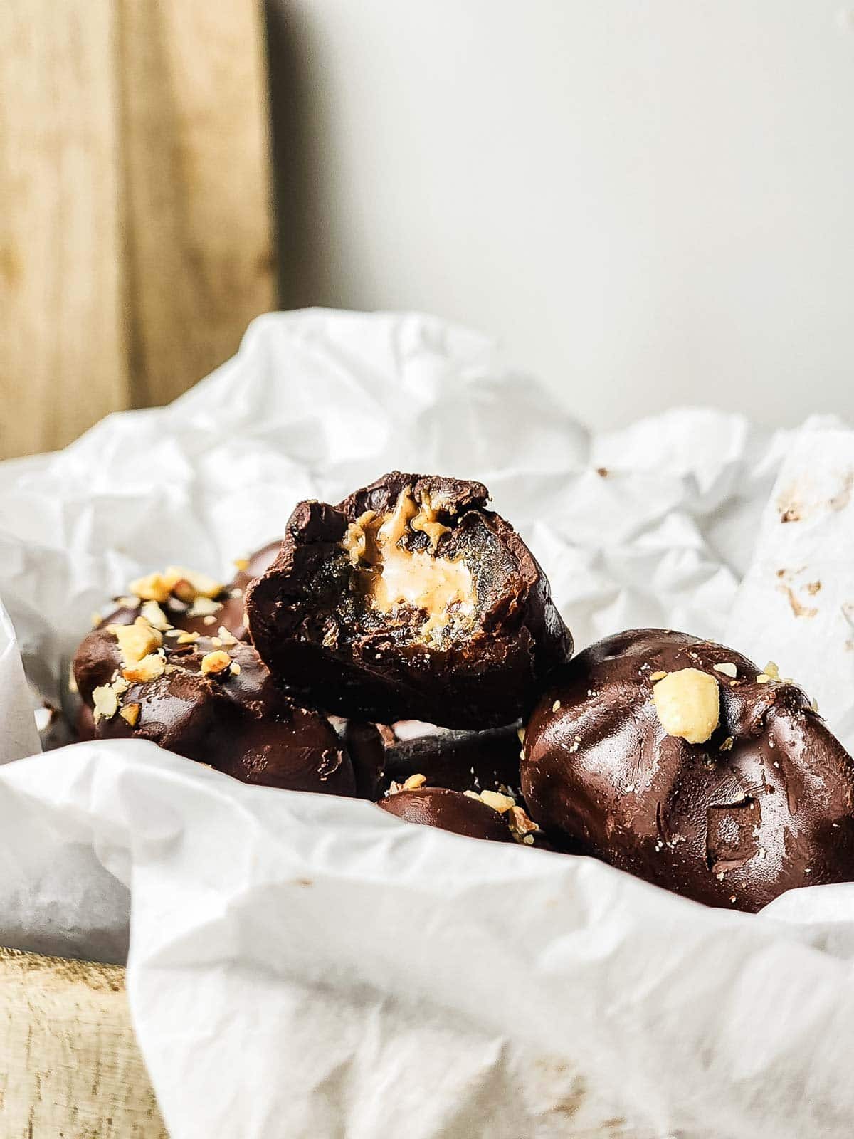 Chocolate-covered treats with a creamy peanut butter filling, topped with chopped nuts, on crumpled parchment paper.