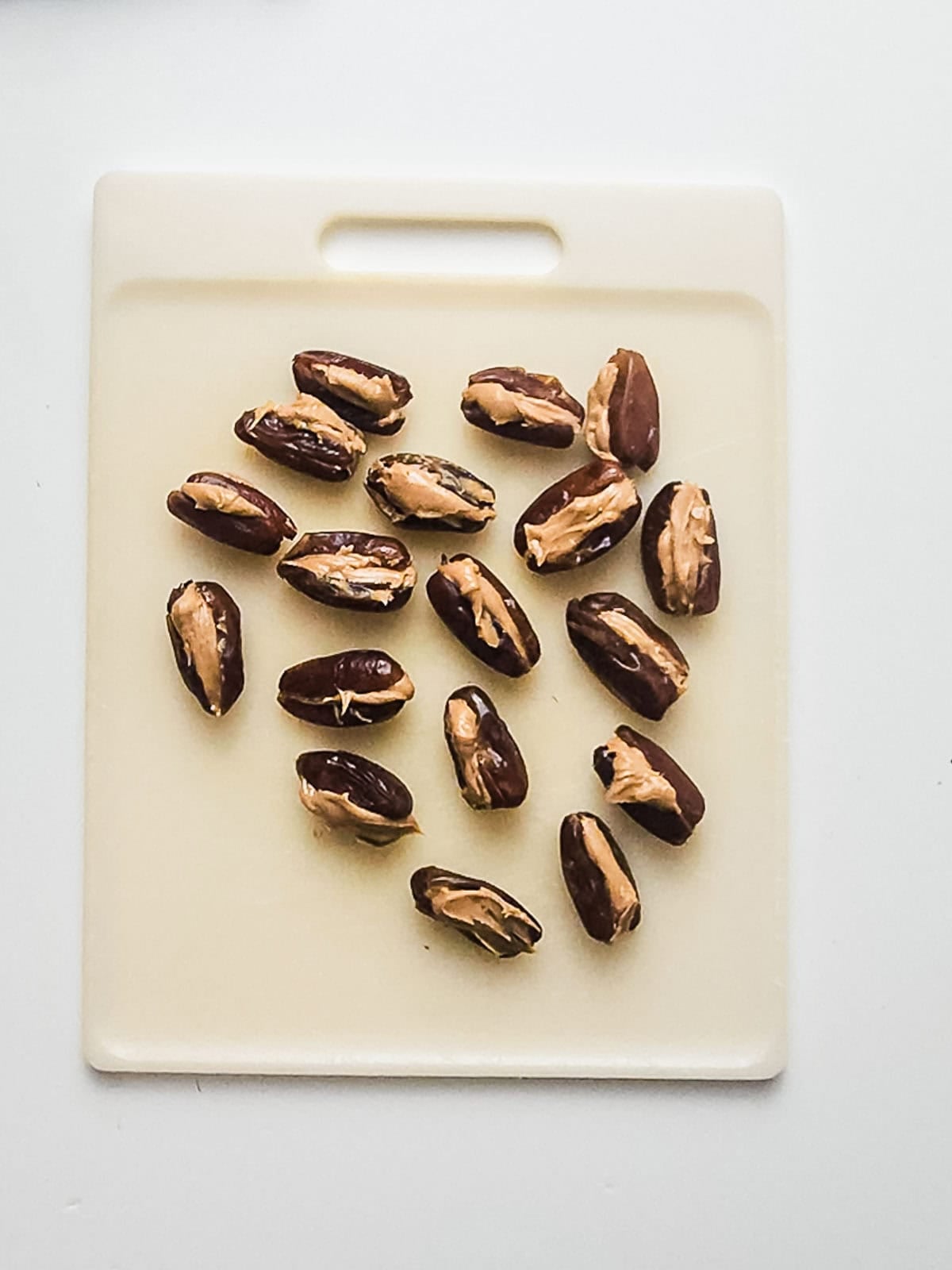 Dates stuffed with peanut butter arranged on a white cutting board against a white background.