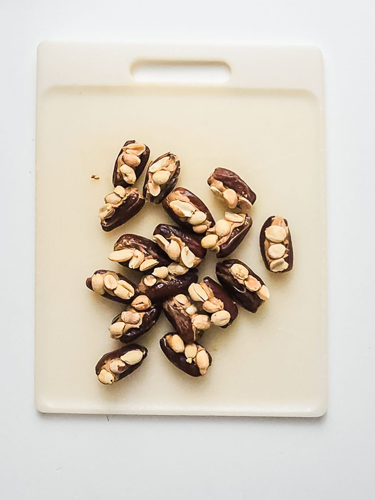 Dates stuffed with peanuts arranged on a white plastic cutting board.