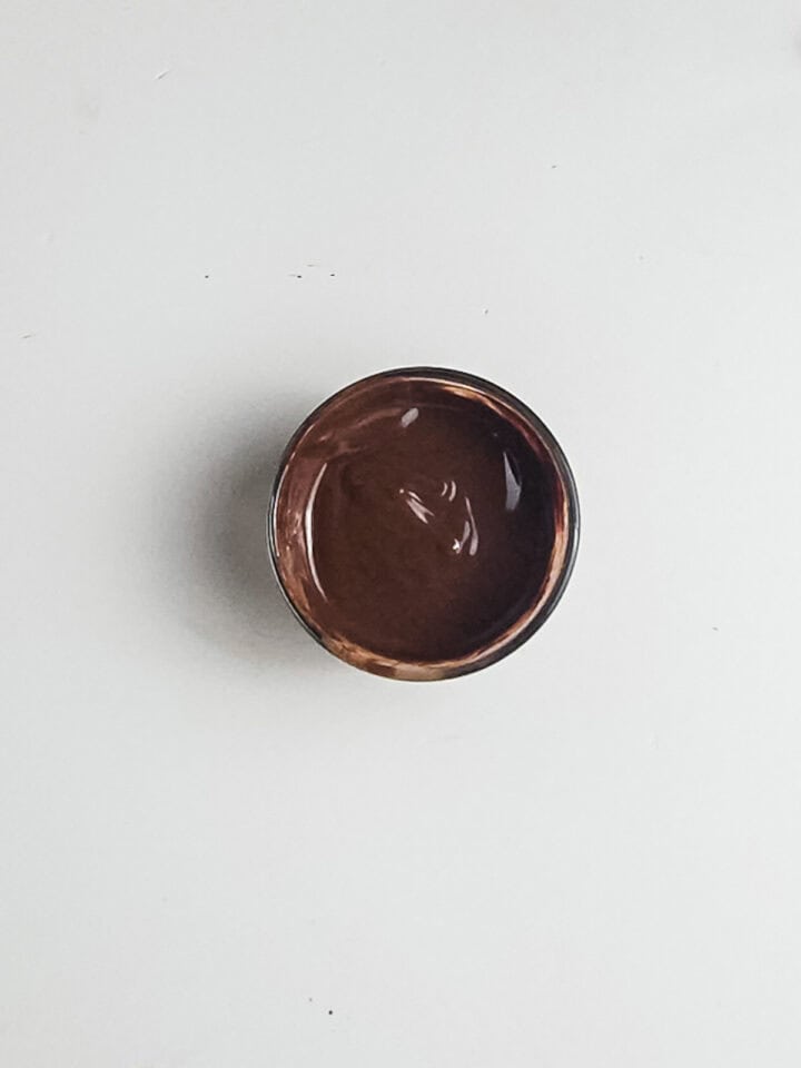 A small bowl filled with chocolate sauce on a white background.