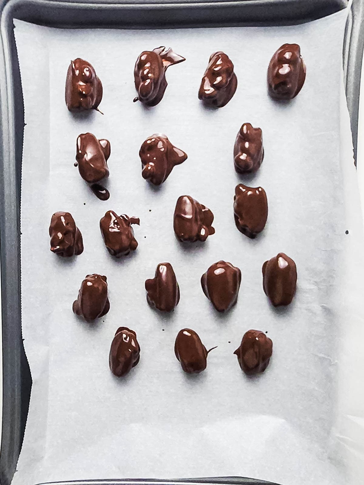 Chocolate-covered clusters on a parchment-lined baking sheet, arranged in rows and ready to set.