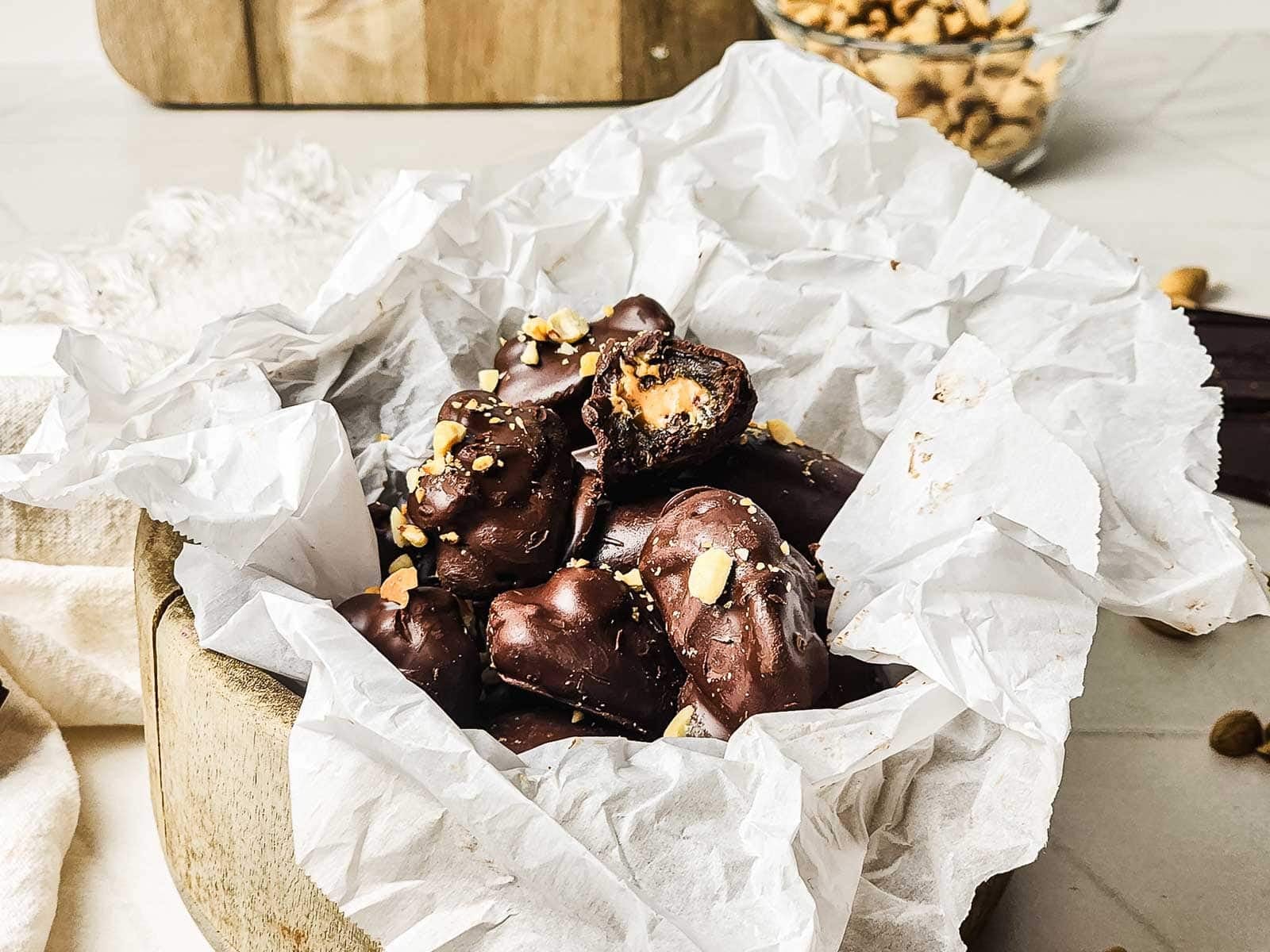 Chocolate-covered dates with nuts, arranged on crumpled parchment paper in a wooden bowl.