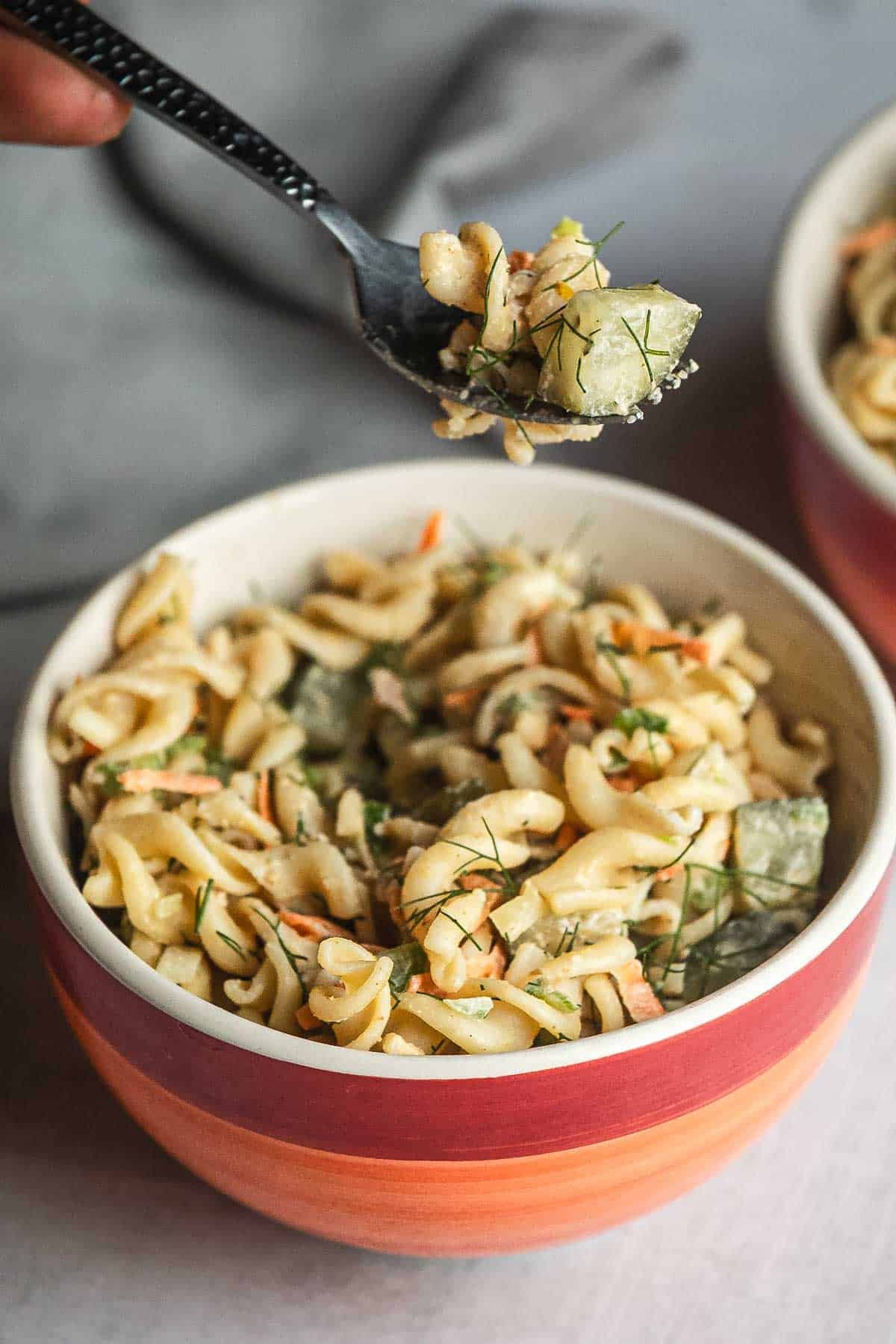 A bowl of creamy Pickle Pasta Salad with vegetables, with a spoon lifting a bite above the bowl.
