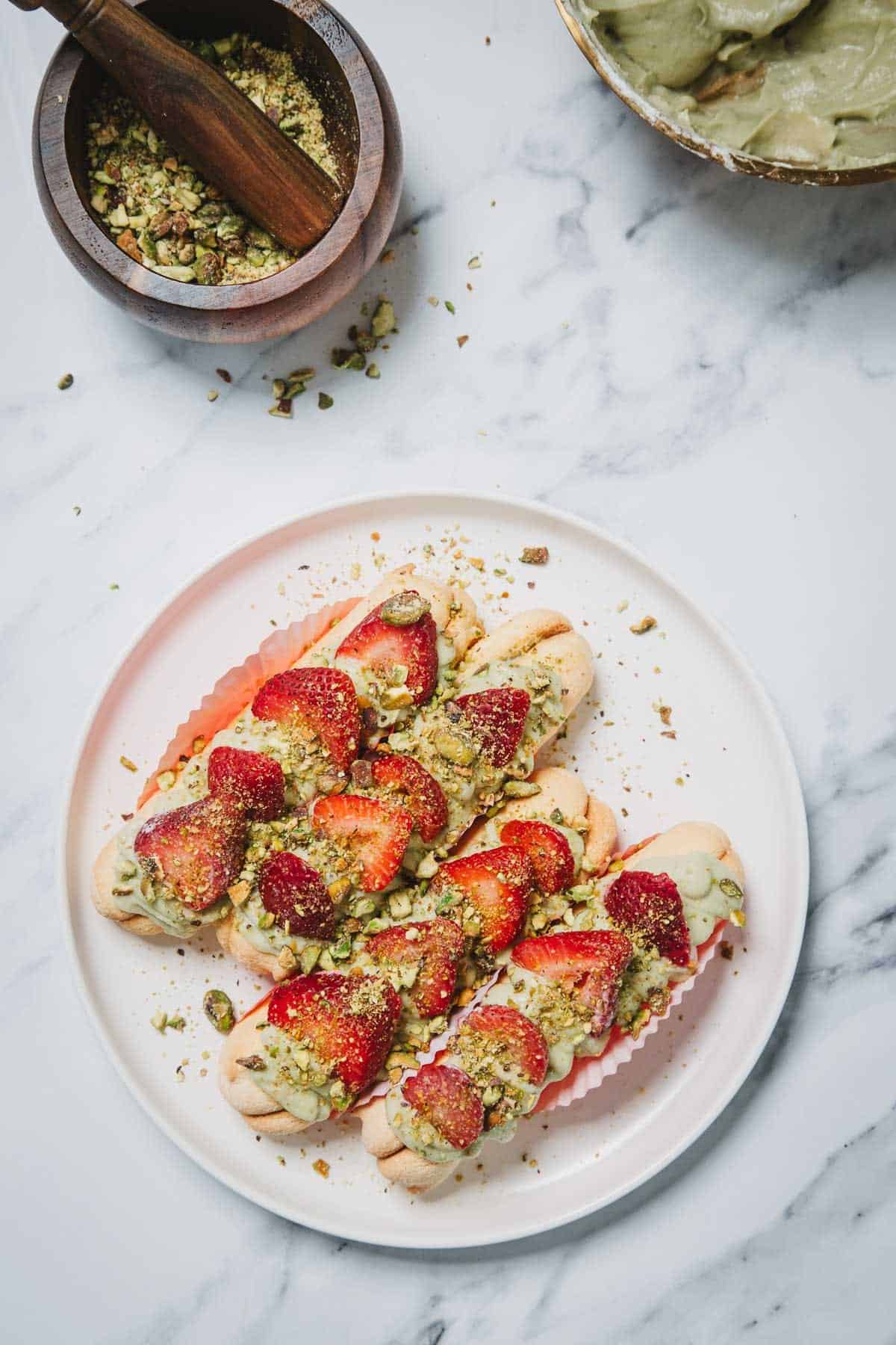 No-Bake Strawberry Pistachio Ladyfingers Dessert featuring ladyfinger cookies topped with green pistachio cream, sliced strawberries, and crushed pistachios on a plate.