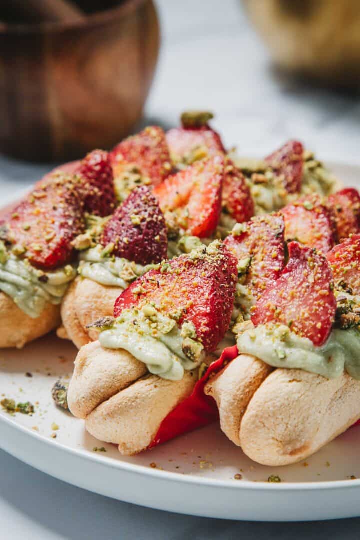 Ladyfinger cookies topped with green cream, sliced strawberries, and crushed pistachios on a white plate.