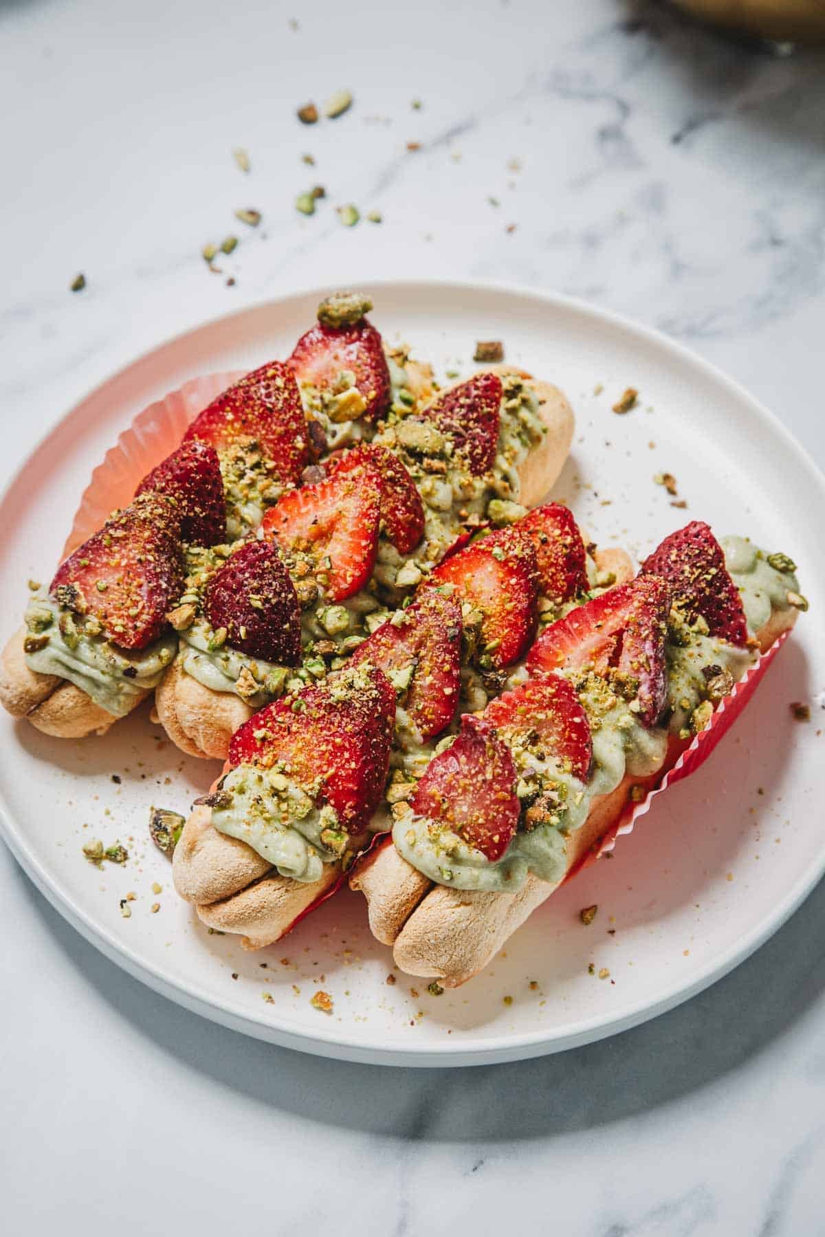 No-Bake Strawberry Pistachio Ladyfingers Dessert features ladyfingers topped with green cream, fresh strawberries, and crushed pistachios on a white plate.