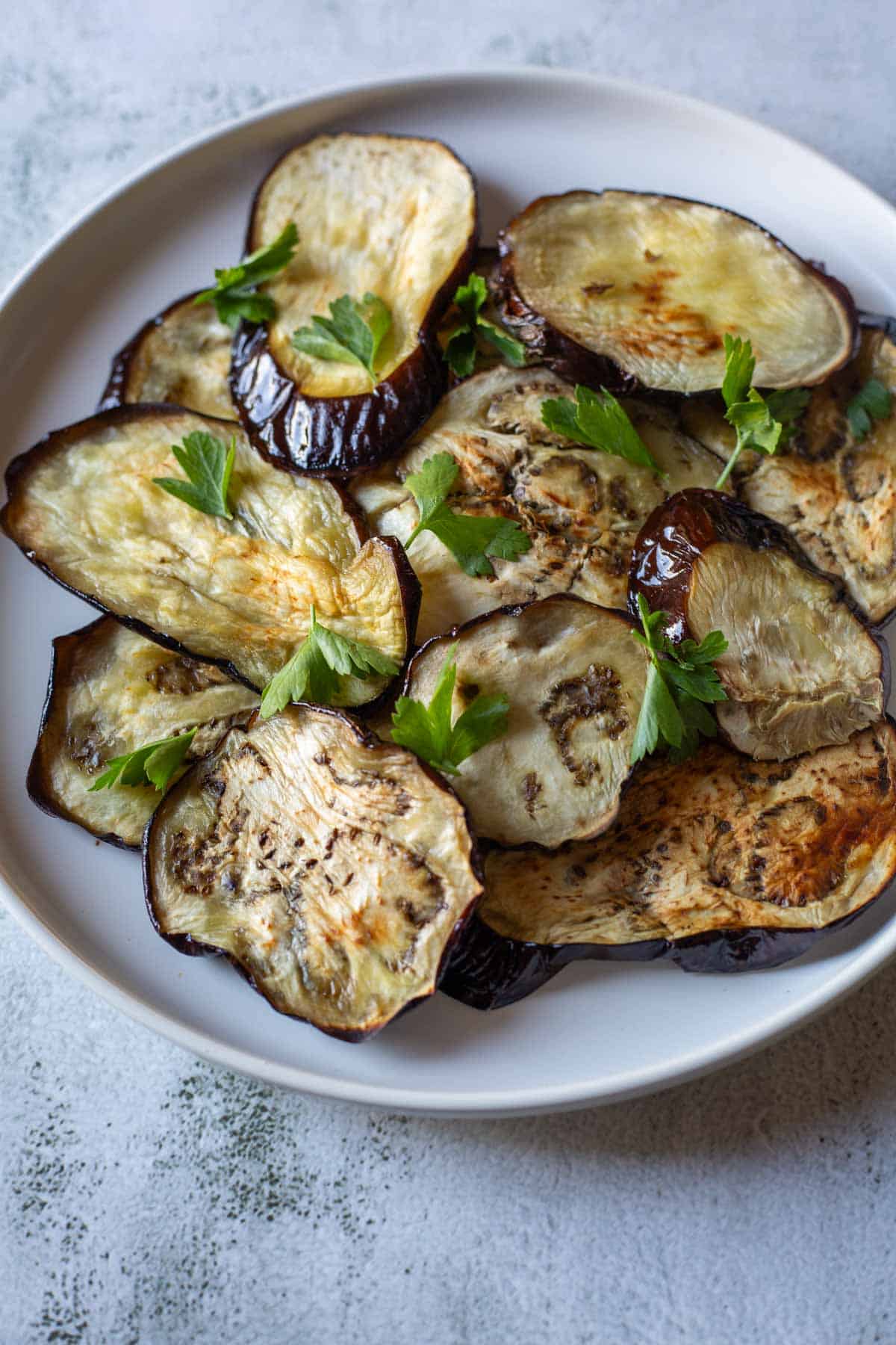 A white plate with slices of air fryer eggplant garnished with fresh parsley.