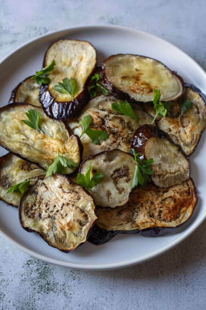 Slices of roasted air fryer eggplant on a white plate, garnished with fresh parsley.