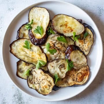 Sliced air fryer eggplant on a white plate, garnished with fresh parsley leaves.