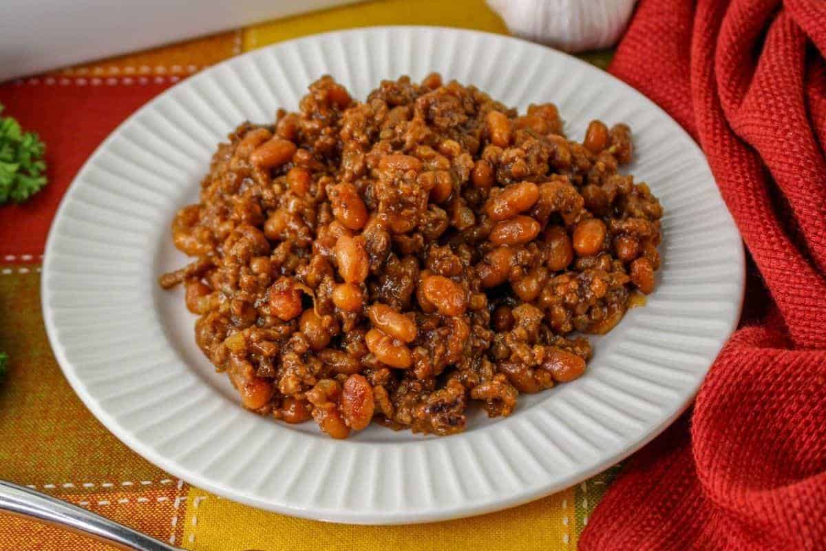 A white plate filled with baked beans and ground beef, placed on a colorful tablecloth.
