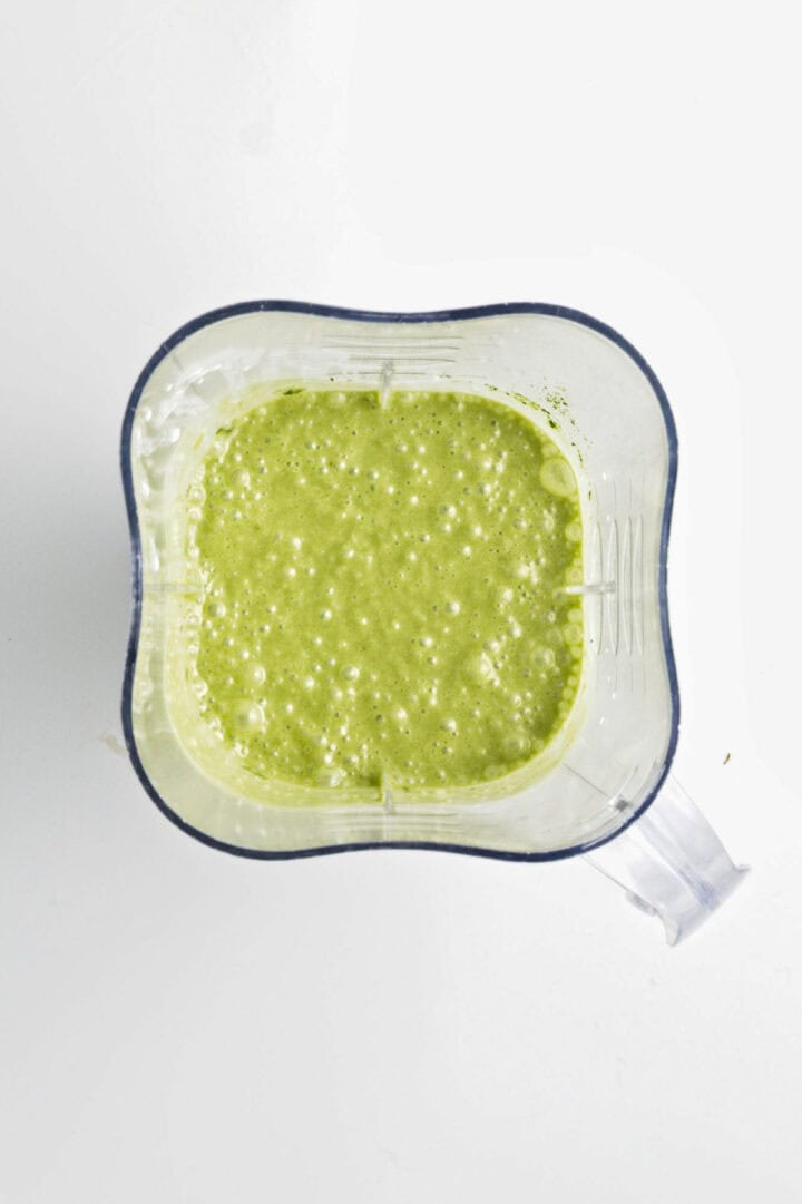 Overhead view of a blender filled with frothy, blended green smoothie on a white background, perfect for making Banana Matcha Chia Pudding.