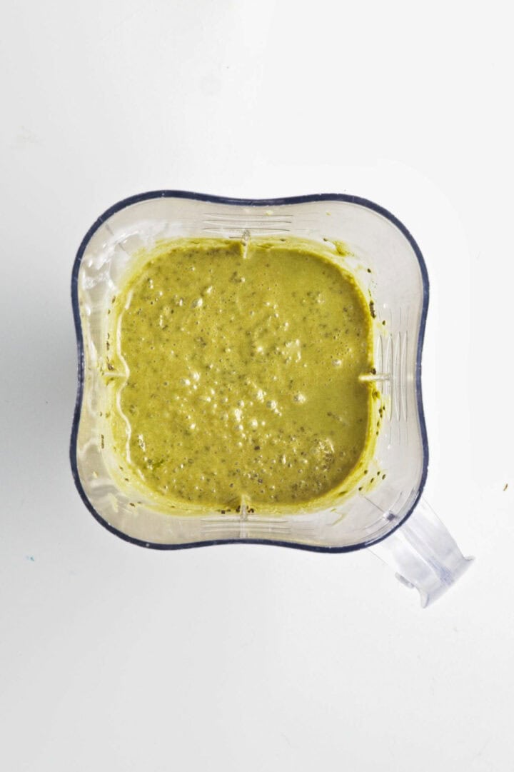 Blended green sauce with herbs and spices in a clear blender container, viewed from above&mdash;reminiscent of the vibrant hue found in Banana Matcha Chia Pudding.