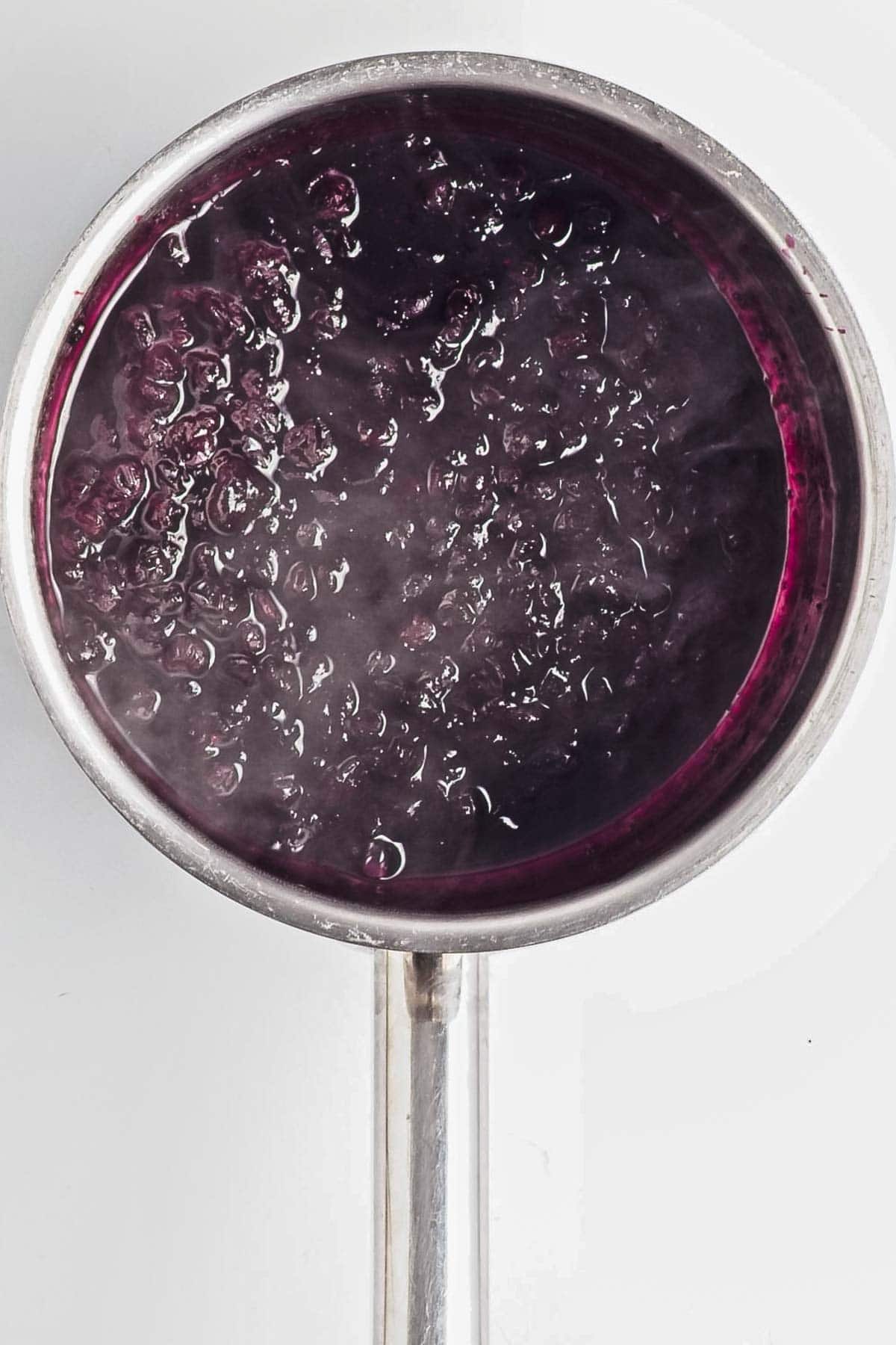 A pot of bubbling dark purple liquid, possibly fruit jam or the beginnings of a rich Berry Chia Pudding, seen from above.