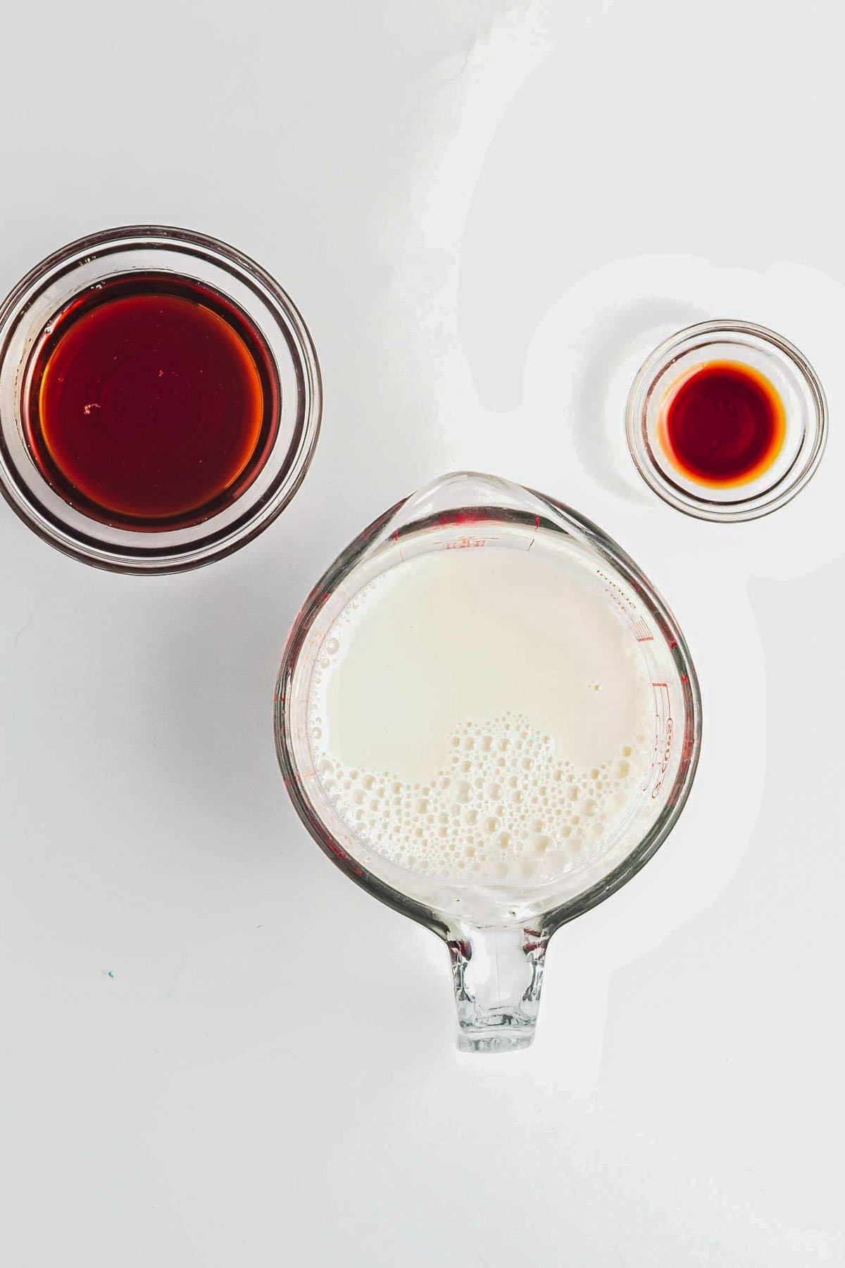 Overhead view of three glass containers with milk, coffee, and vanilla extract on a white background-perfect ingredients to complement a delicious Berry Chia Pudding.