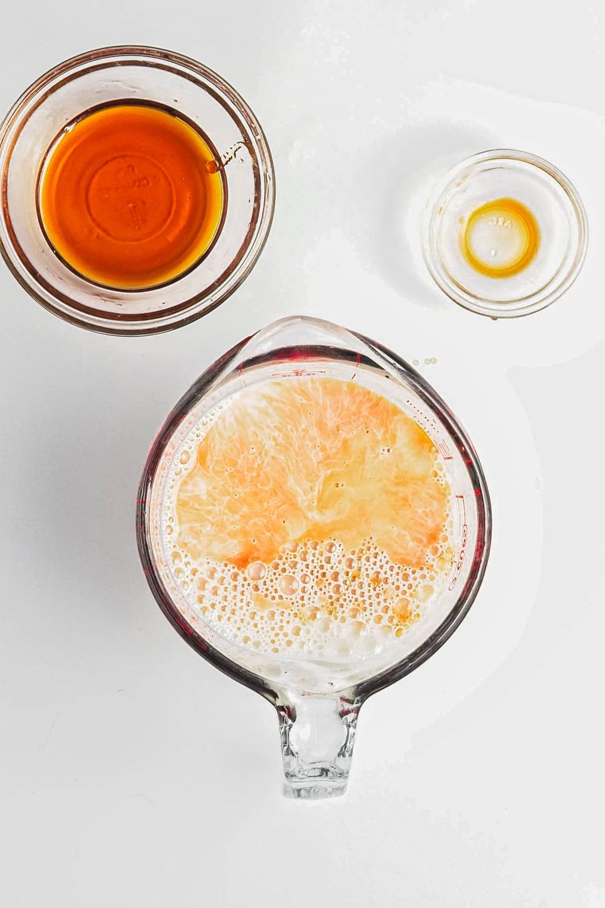 A glass measuring cup with foamy milk and honey, next to small bowls of honey and vanilla extract-perfect ingredients for crafting a Berry Chia Pudding.