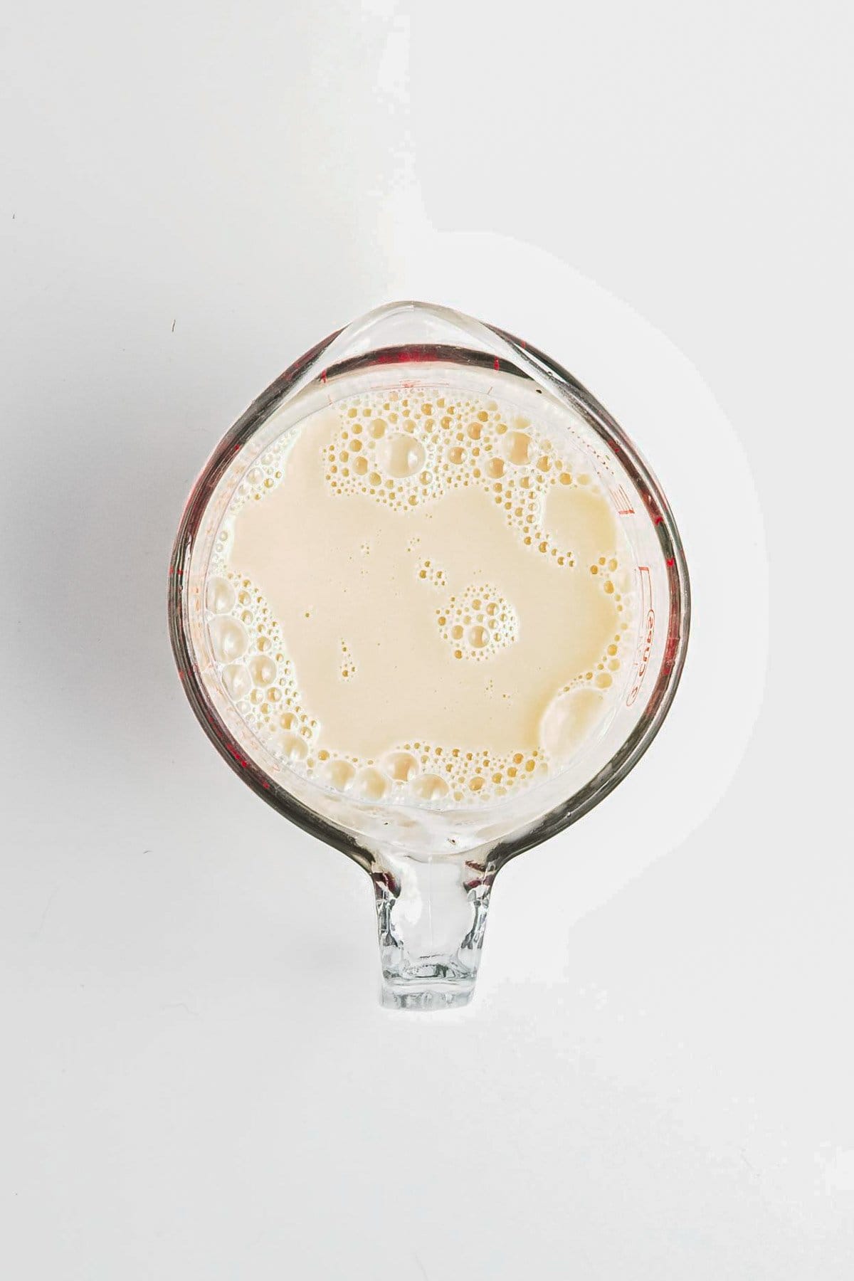A glass measuring cup filled with a frothy, creamy liquid-perhaps the start of a luscious Berry Chia Pudding-viewed from above on a white background.