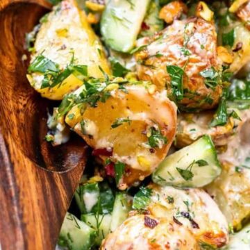 Close-up of creamy potato salad with herbs and cucumber in a wooden spoon on a plate.