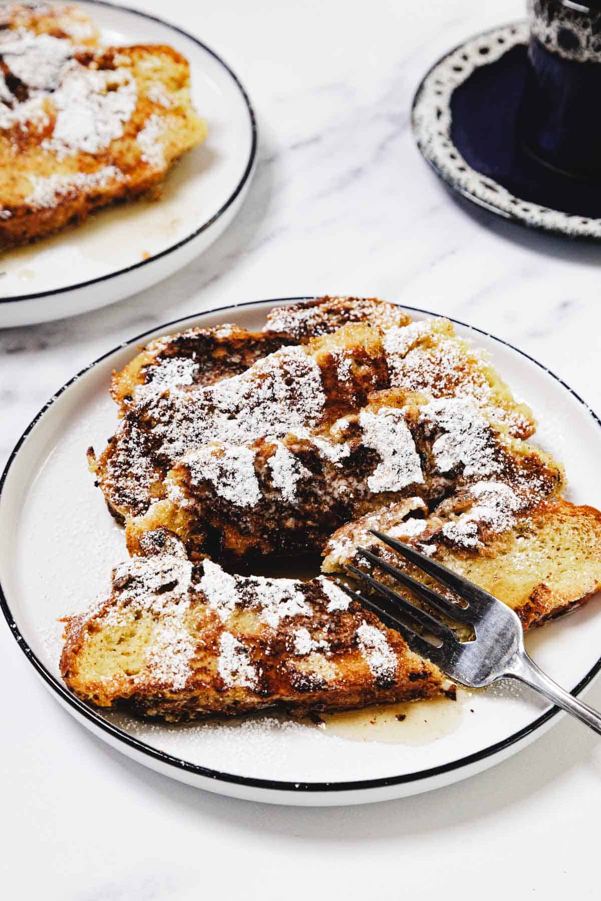 Plate of Challah French Toast slices dusted with powdered sugar, with a fork resting on the side.