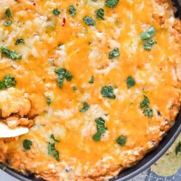 Cheesy baked dip in a skillet, topped with cilantro, served with tortilla chips and lime on the side.