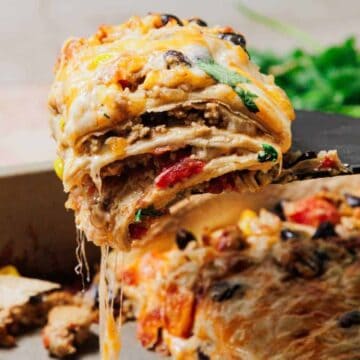 A cheesy, layered slice of casserole is being lifted from a baking dish, with melted cheese stretching.