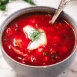 Bowl of hearty Chicken Borscht soup with sour cream, fresh dill, and a spoon on a marble surface.