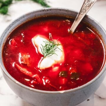 Bowl of hearty Chicken Borscht soup with sour cream, fresh dill, and a spoon on a marble surface.