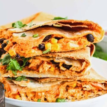 Stacked quesadillas filled with cheese, black beans, and veggies on a white plate, garnished with cilantro.