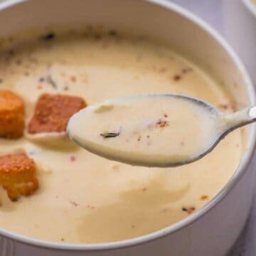 A spoonful of creamy soup with croutons and herbs in a white bowl.