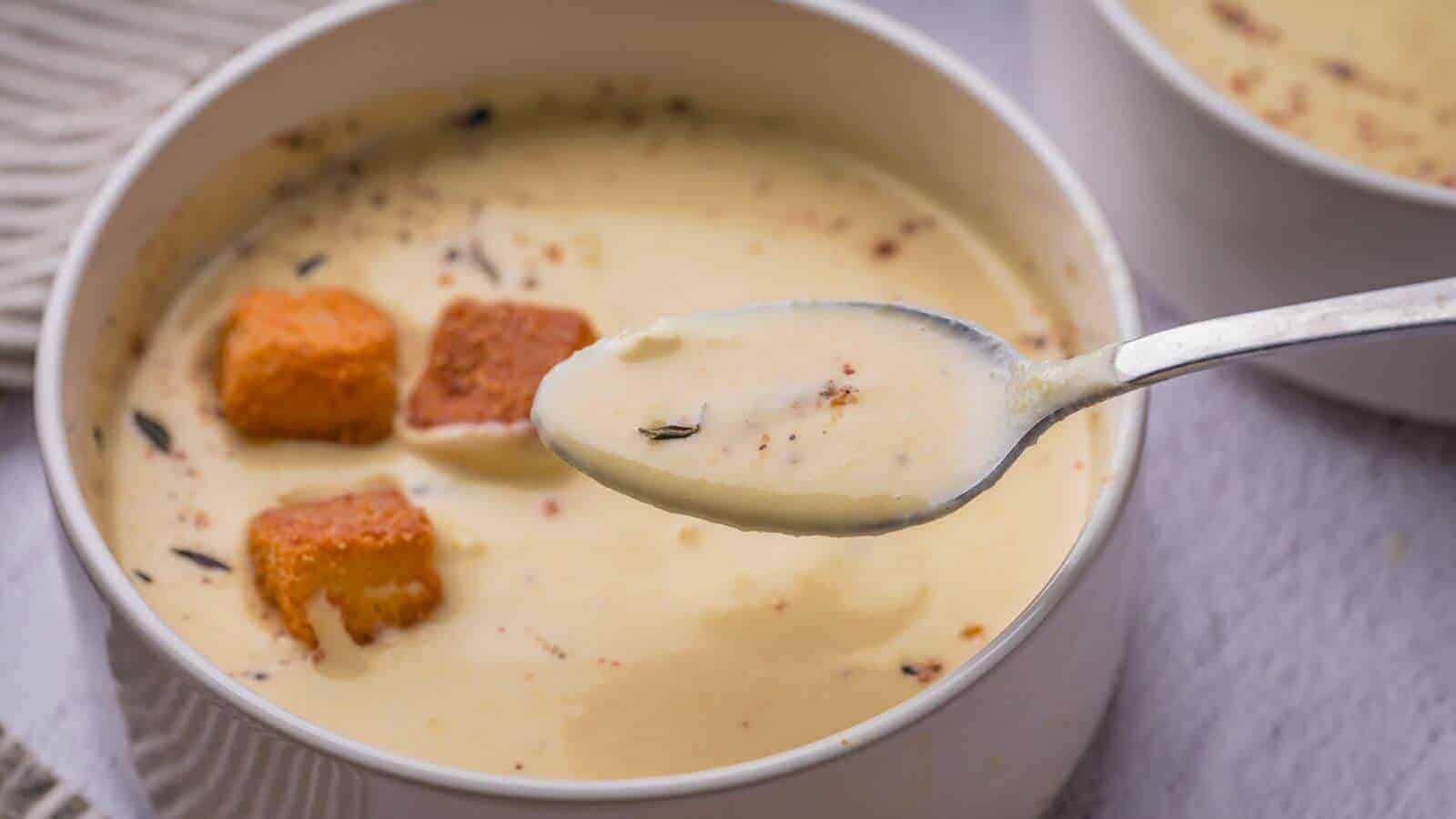 A spoonful of creamy soup with croutons and herbs in a white bowl.