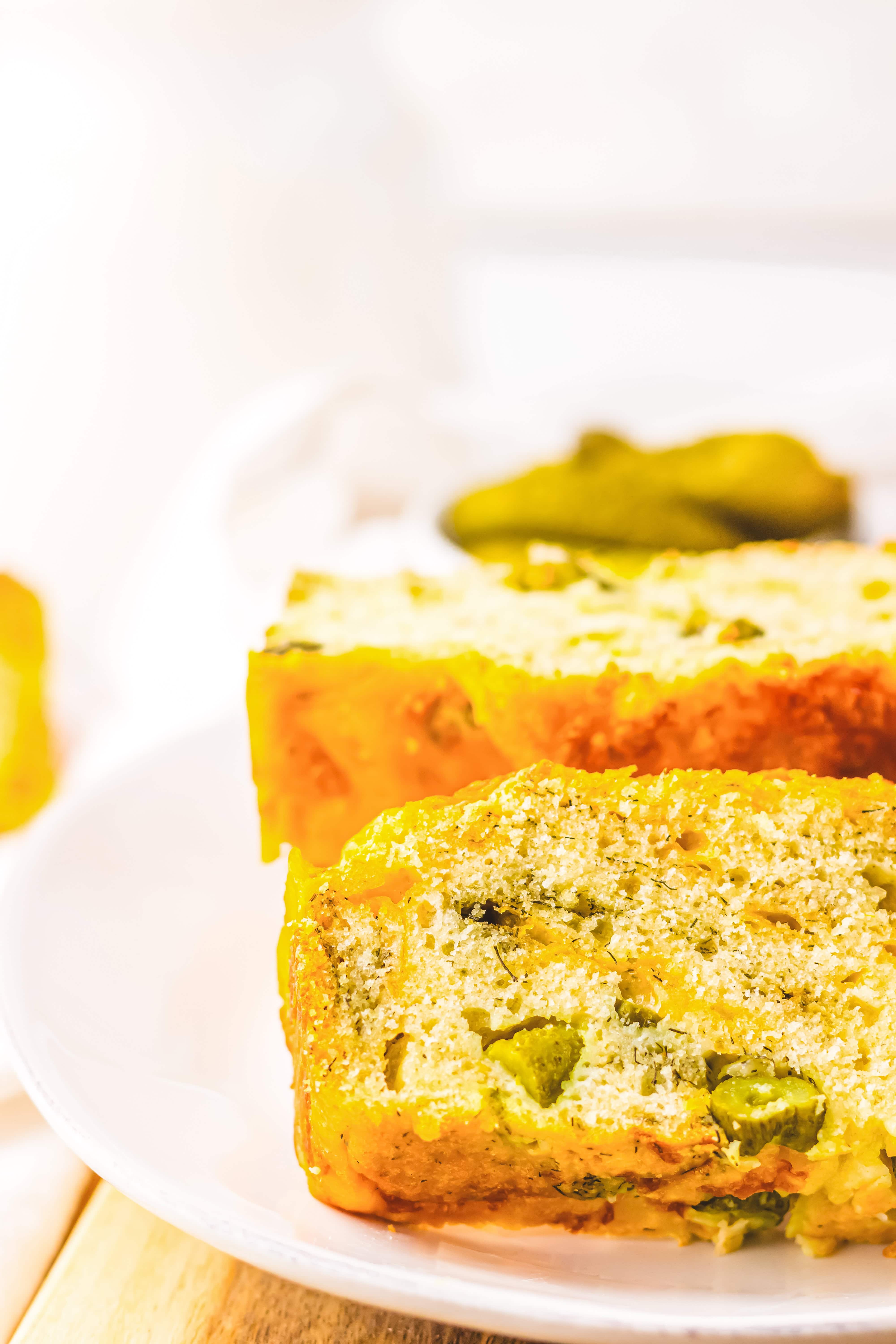 Close-up of two slices of savory Dill Pickle Bread with green vegetables, served on a white plate.