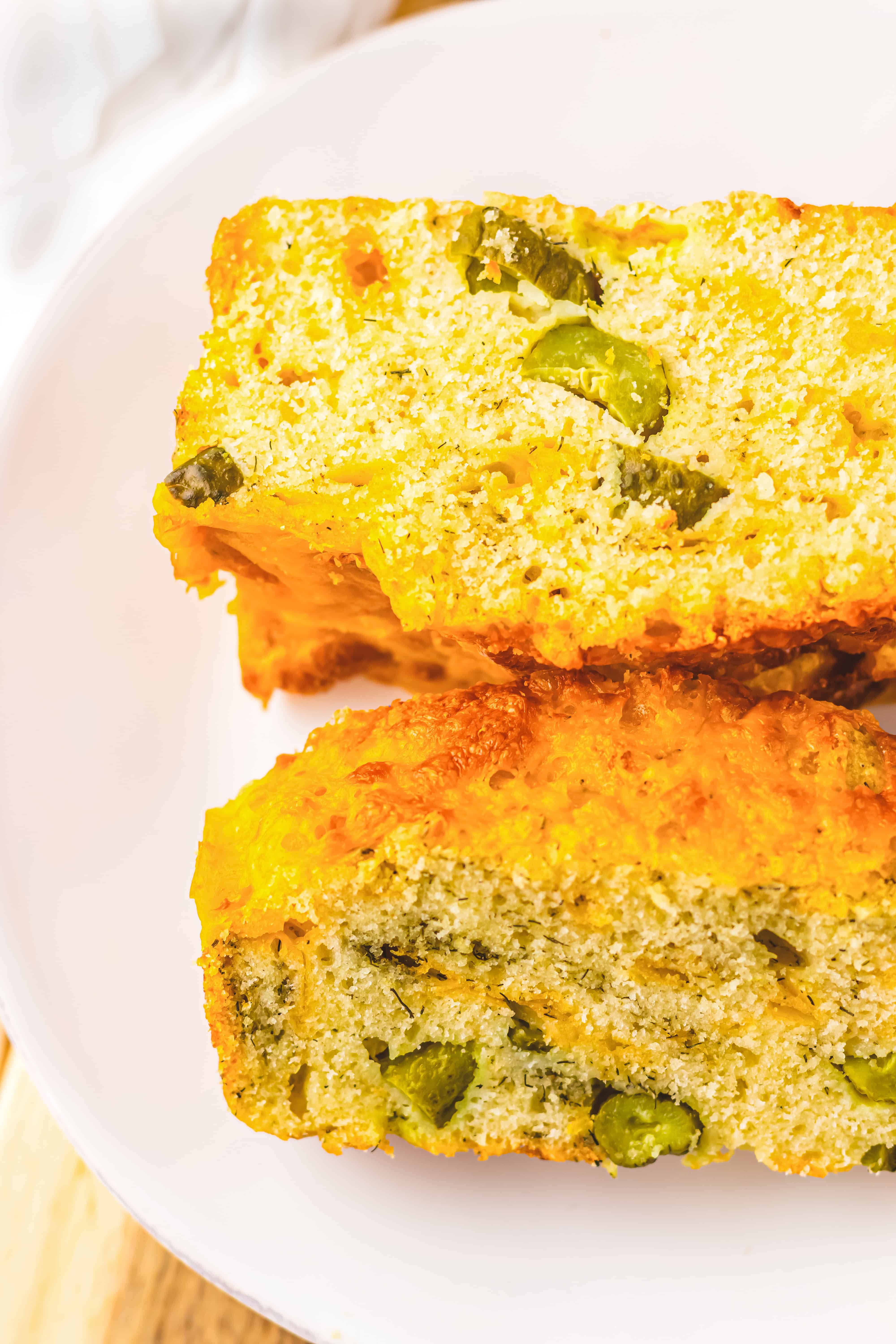 Two slices of savory Dill Pickle Bread with green olives and herbs sit on a white plate.