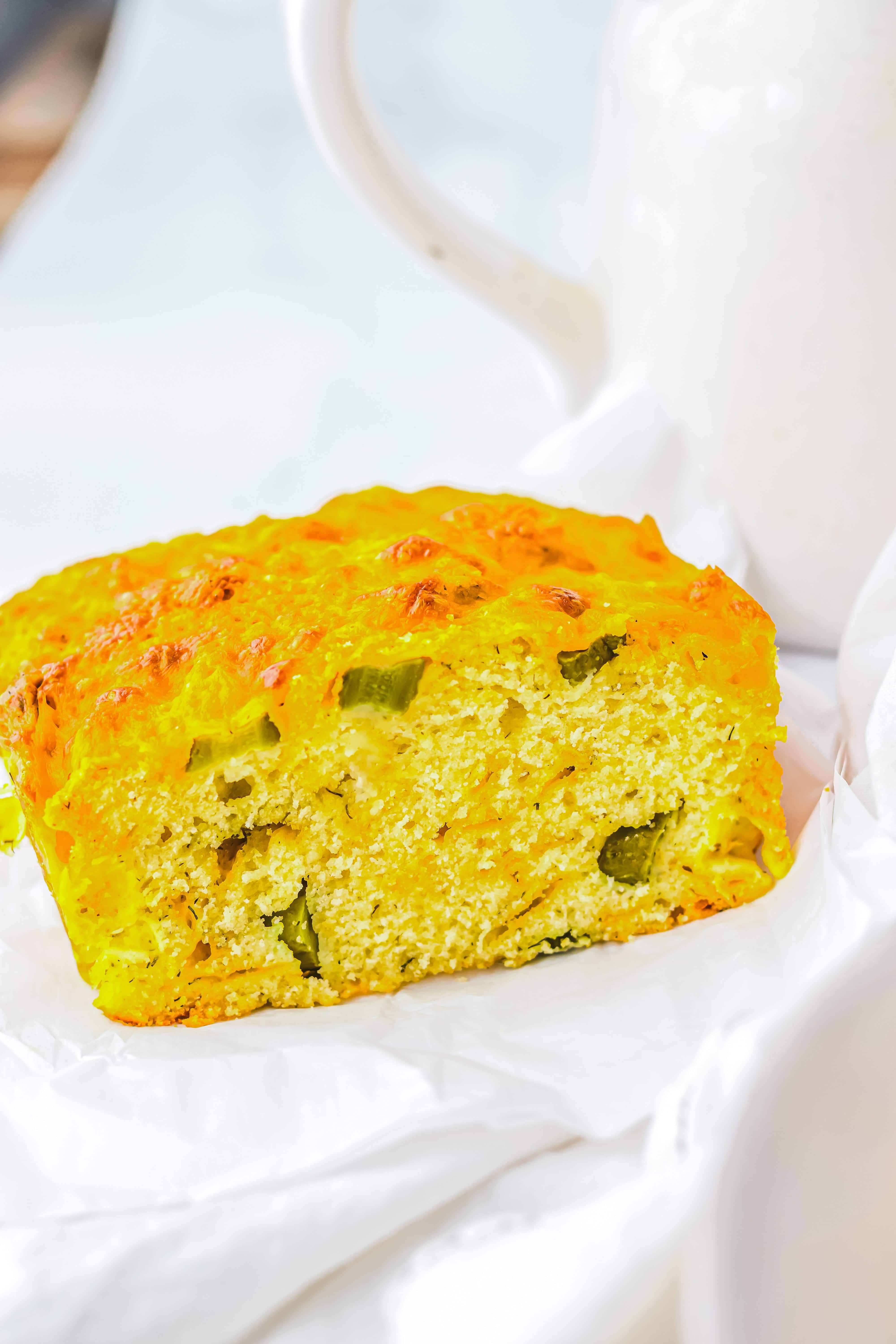 A slice of yellow Dill Pickle Bread with green pepper pieces, placed on white parchment paper.