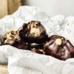 Chocolate-covered candies with a creamy filling and nut pieces on top, placed on crumpled white parchment paper.
